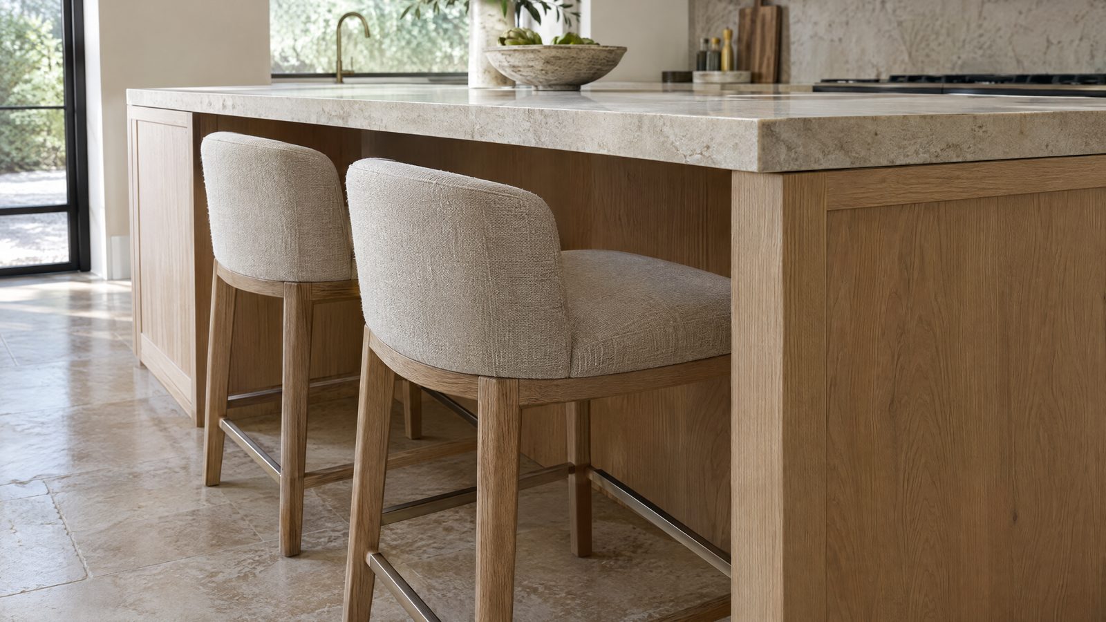 Seating side of a kitchen island: a thick light stone countertop overhangs white-oak panels, with two counter stools tucked into the knee space